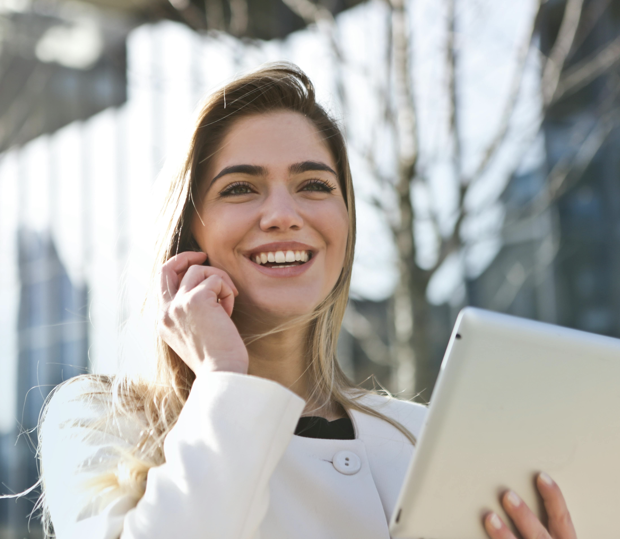 Femme souriante utilisant une tablette à l’extérieur, symbole de confiance et de réussite professionnelle.