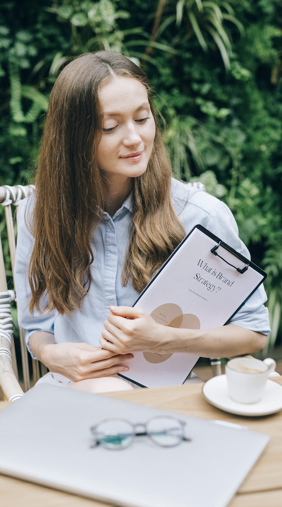 Jeune femme tenant un dossier intitulé « What is Brand Strategy ? » en terrasse.