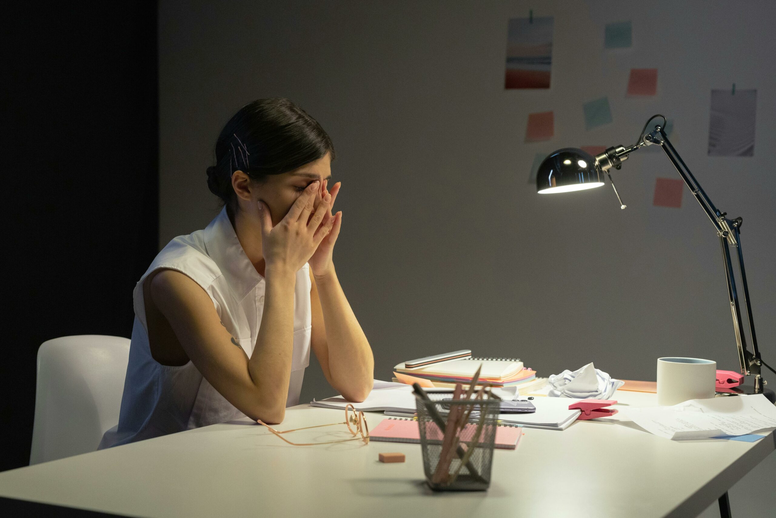 Femme assise à son bureau, le visage entre les mains, exprimant de la fatigue et du stress au travail.