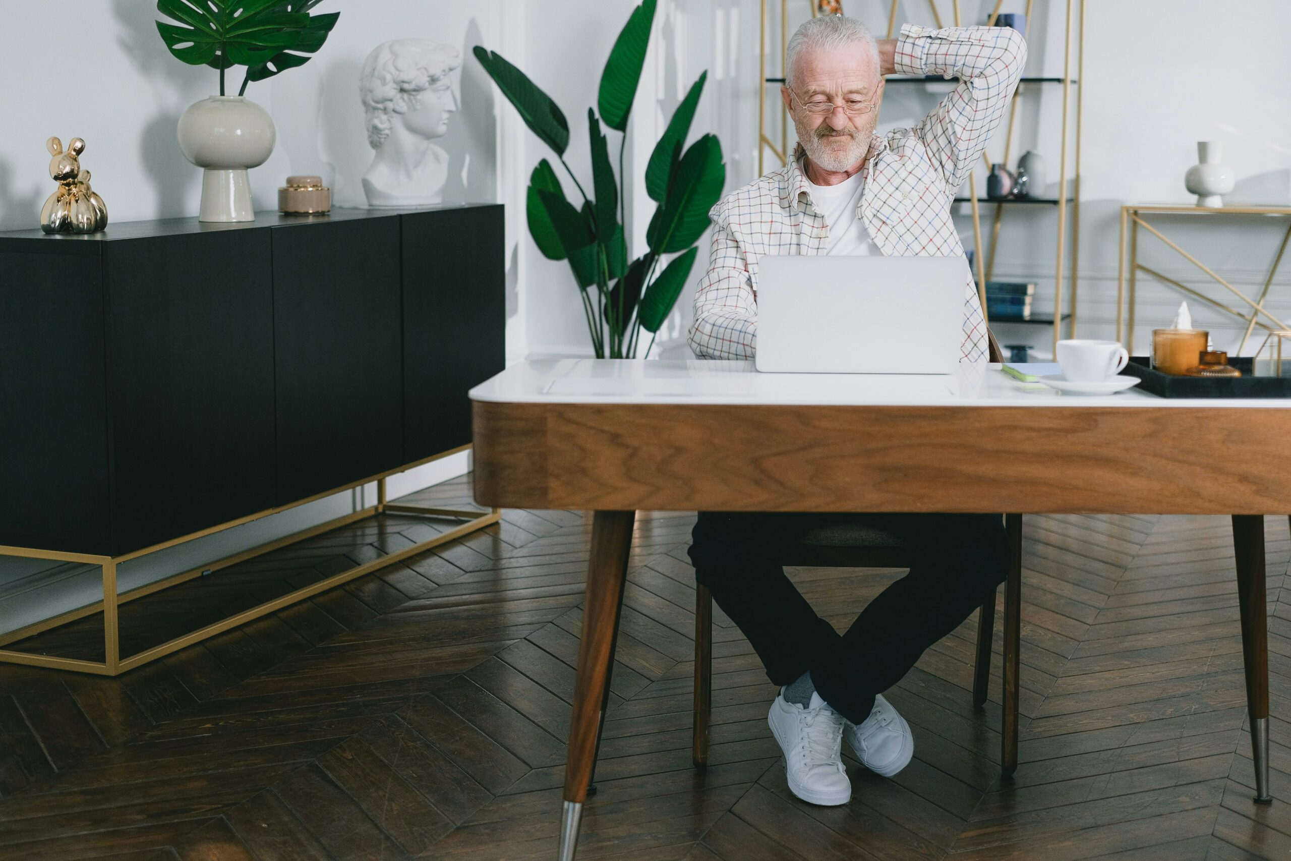 Homme âgé assis à son bureau, utilisant un ordinateur portable, l’air concentré et légèrement fatigué.
